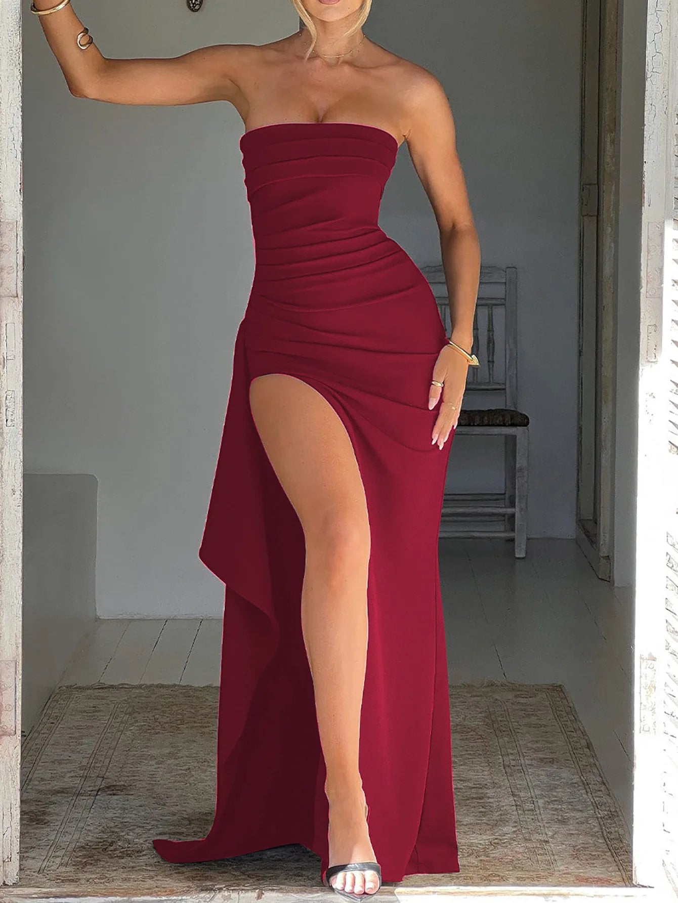 Woman wearing a strapless red dress with a high slit, standing in a doorway.