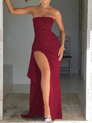 Woman wearing a strapless red dress with a high slit, standing in a doorway.